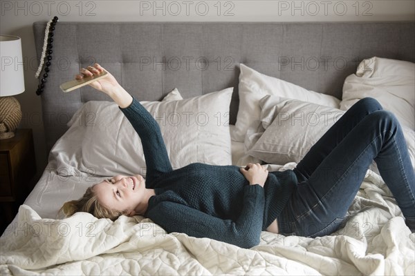 Woman laying on bed posing for cell phone selfie