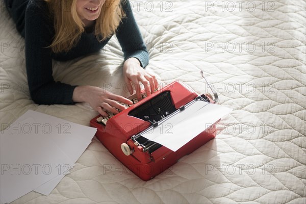 Smiling woman laying on bed typing on typewriter