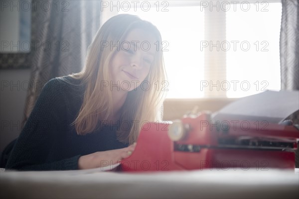 Smiling woman laying on bed typing on typewriter