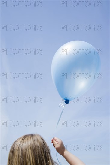 Caucasian girl holding blue balloon in blue sky