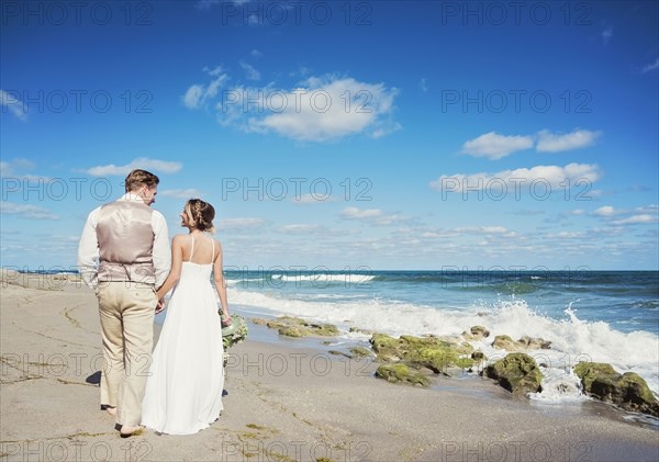 Caucasian bride and groom walking on beach