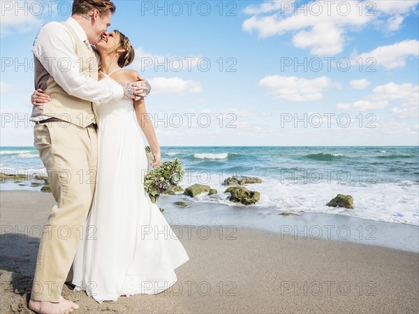 Caucasian bride and groom hugging on beach