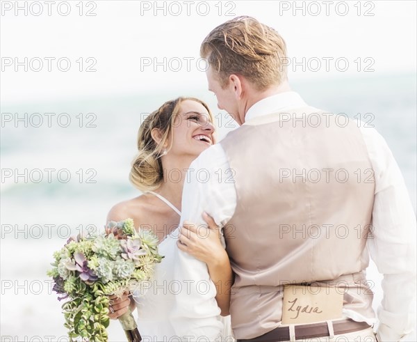 Caucasian bride and groom hugging on beach