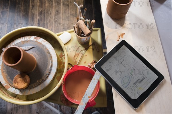 Cup and tools on pottery wheel near digital tablet