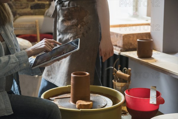 Caucasian women using digital tablet near pottery wheel