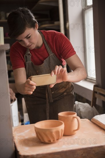 Caucasian woman photographing pottery with cell phone