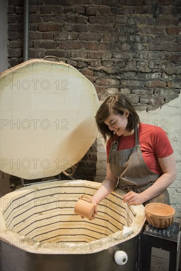 Smiling Caucasian woman placing cup in pottery kiln