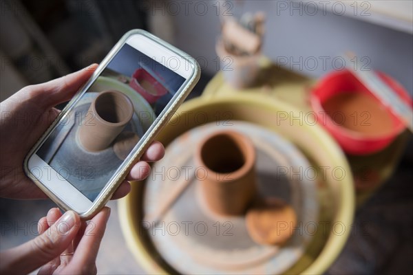 Hands of Caucasian woman photographing pottery with cell phone