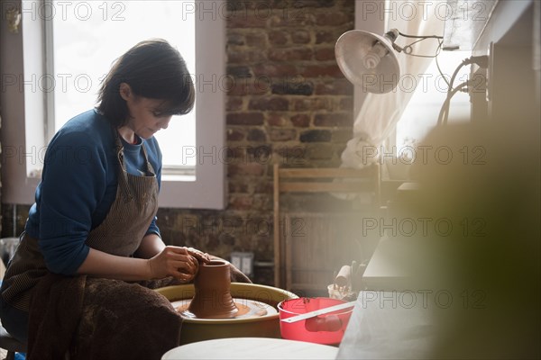 Caucasian woman shaping clay on pottery wheel