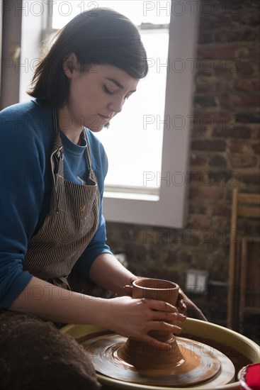 Caucasian woman shaping clay on pottery wheel