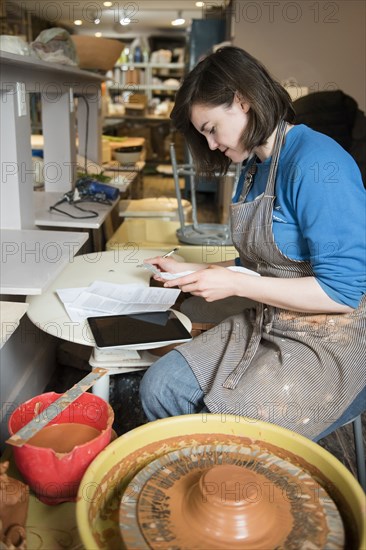 Caucasian woman reading paperwork near pottery wheel