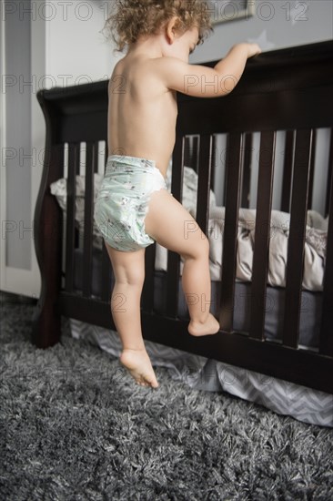 Caucasian boy wearing diaper climbing on bed frame