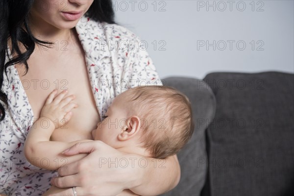 Caucasian mother breastfeeding baby son on sofa