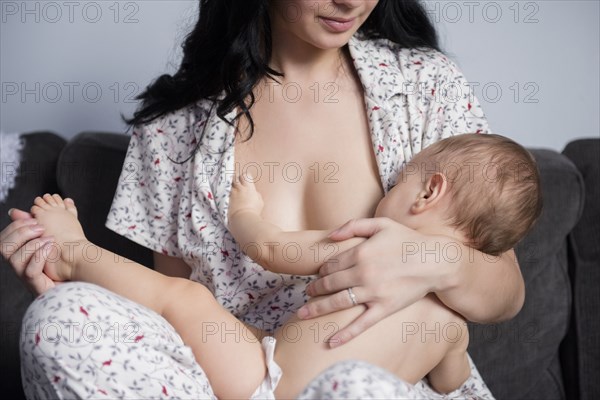 Caucasian mother breastfeeding baby son on sofa