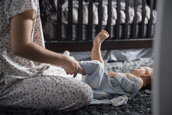 Caucasian mother dressing baby son on floor