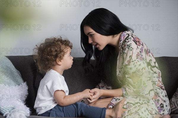 Caucasian mother sitting on sofa holding hands and talking with son