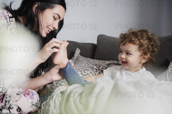 Caucasian mother sitting on sofa playing with toes of son