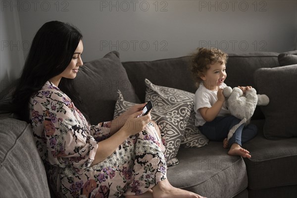 Caucasian mother texting on cell phone sitting on sofa near son