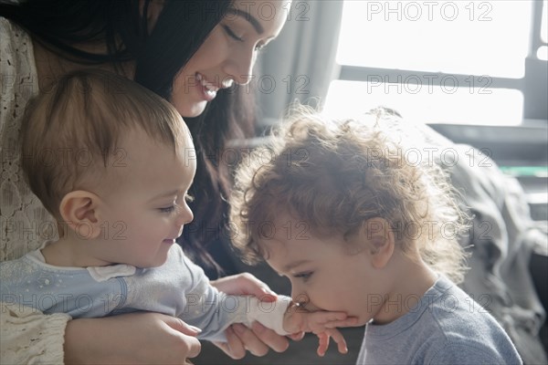 Caucasian mother watching son kiss hand of baby brother