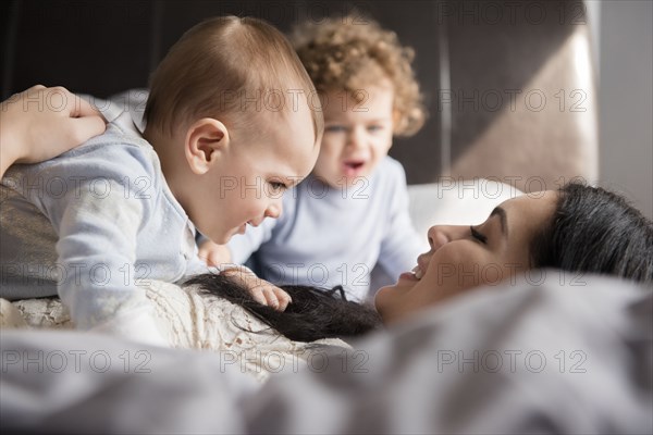 Caucasian mother laying on bed playing with sons