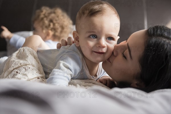 Caucasian mother laying on bed kissing baby son