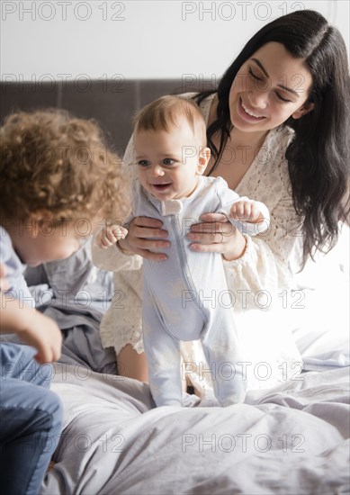 Caucasian mother kneeling on bed playing with sons
