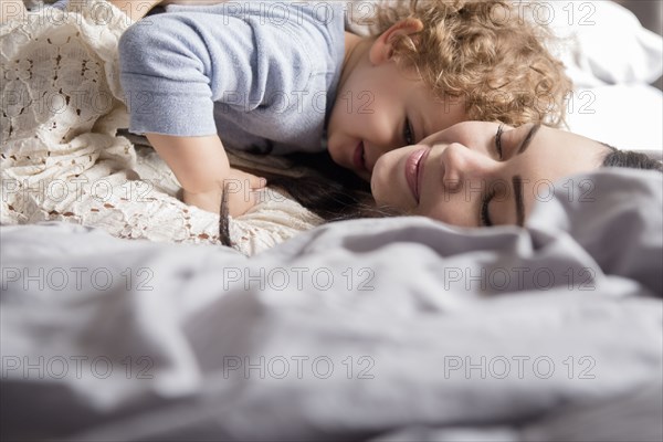 Caucasian mother laying on bed hugging son