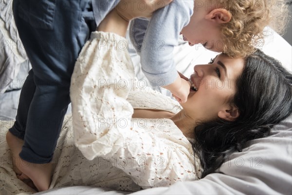 Caucasian mother laying on bed lifting son