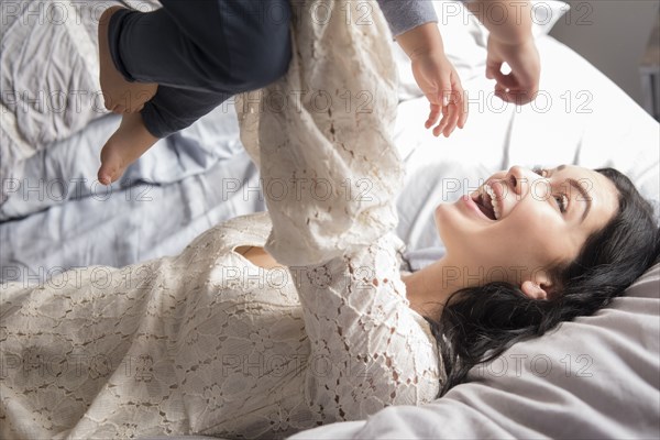 Caucasian mother laying on bed lifting son