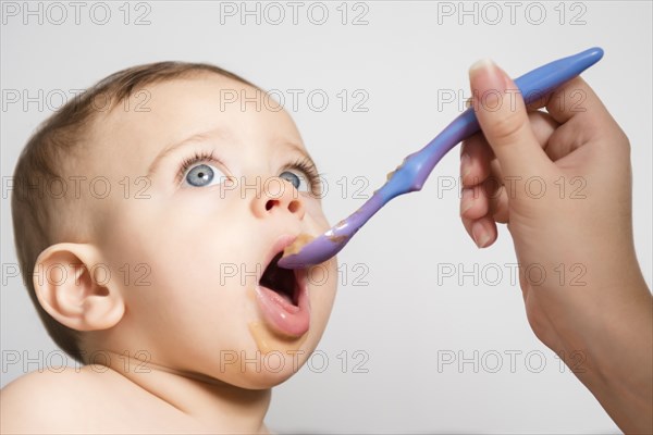 Hand of Caucasian mother feeding baby son with spoon