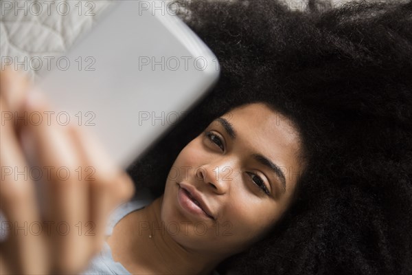 African American woman laying in bed texting on cell phone