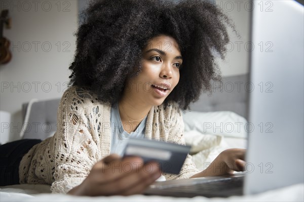 African American woman laying in bed online shopping with laptop