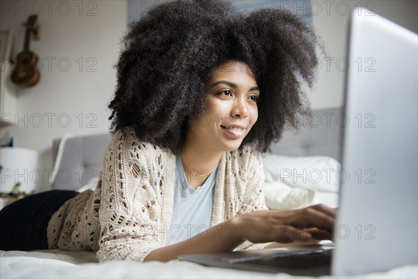 African American woman laying in bed using laptop