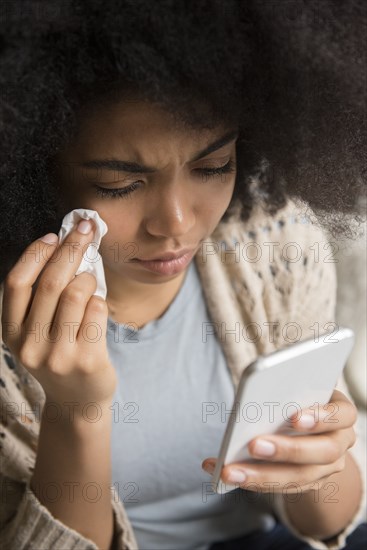 African American woman crying and texting on cell phone