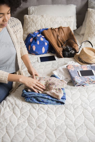 African American woman sitting on bed folding clothing