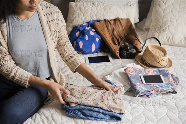 African American woman sitting on bed folding clothing