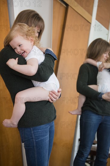 Reflection in mirror of Caucasian mother holding daughter