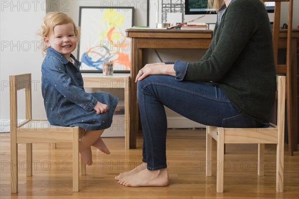 Caucasian mother and daughter sitting on small chairs in home office