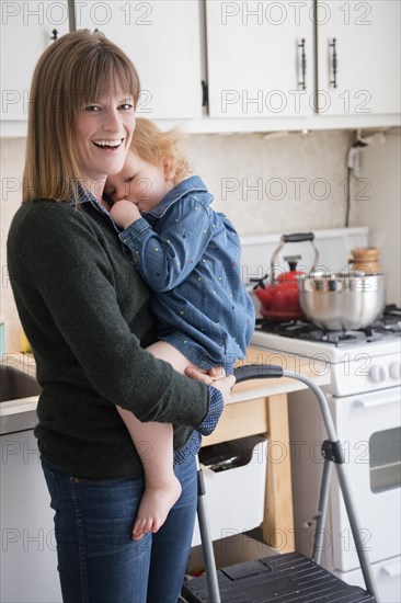 Caucasian mother holding daughter sucking thumb in kitchen