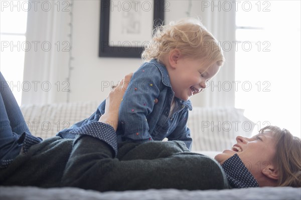 Caucasian mother laying on bed playing with daughter