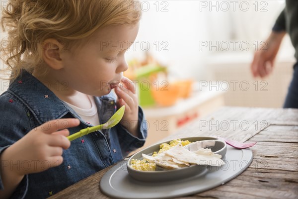 Caucasian girl eating with fingers and spoon