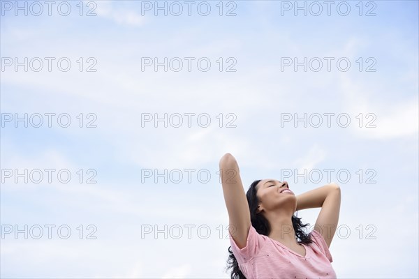 Hispanic woman with hands in hair under cloudy sky