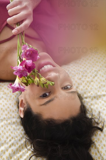 Hispanic woman laying on bed holding flowers