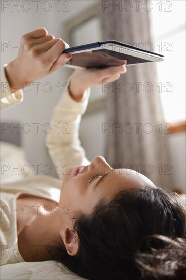 Hispanic woman laying on bed reading digital tablet
