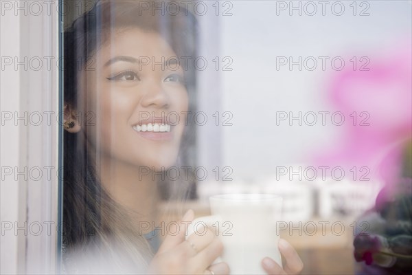 Mixed Race woman drinking coffee behind window