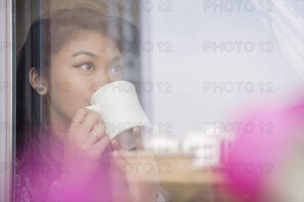 Mixed Race woman drinking coffee behind window