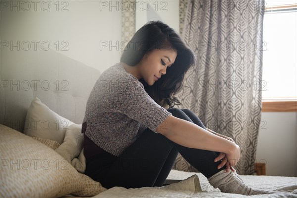 Depressed Mixed Race woman sitting on bed