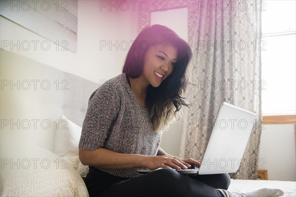 Mixed Race woman sitting on bed using laptop