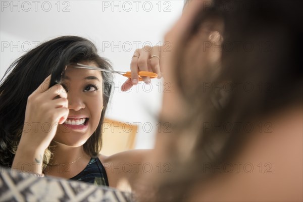 Uncertain Mixed Race woman cutting bangs with scissors