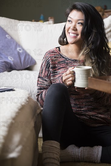 Mixed Race woman sitting on floor drinking coffee